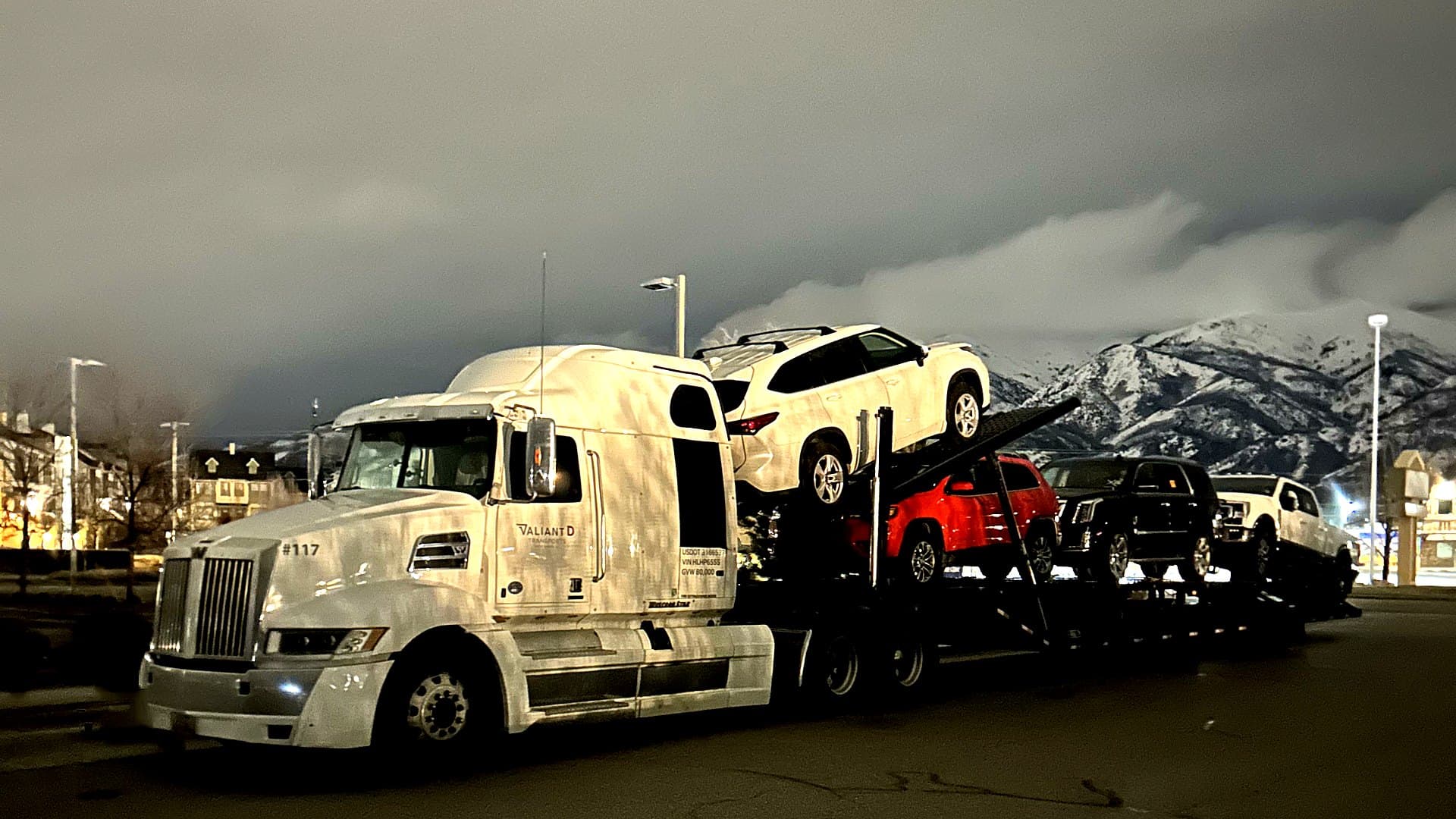 Shipity car carrier hauling vehicles past snow-capped mountains